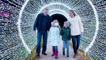 A family of four strolls through a tunnel of glowing lights, enjoying a festive night out.