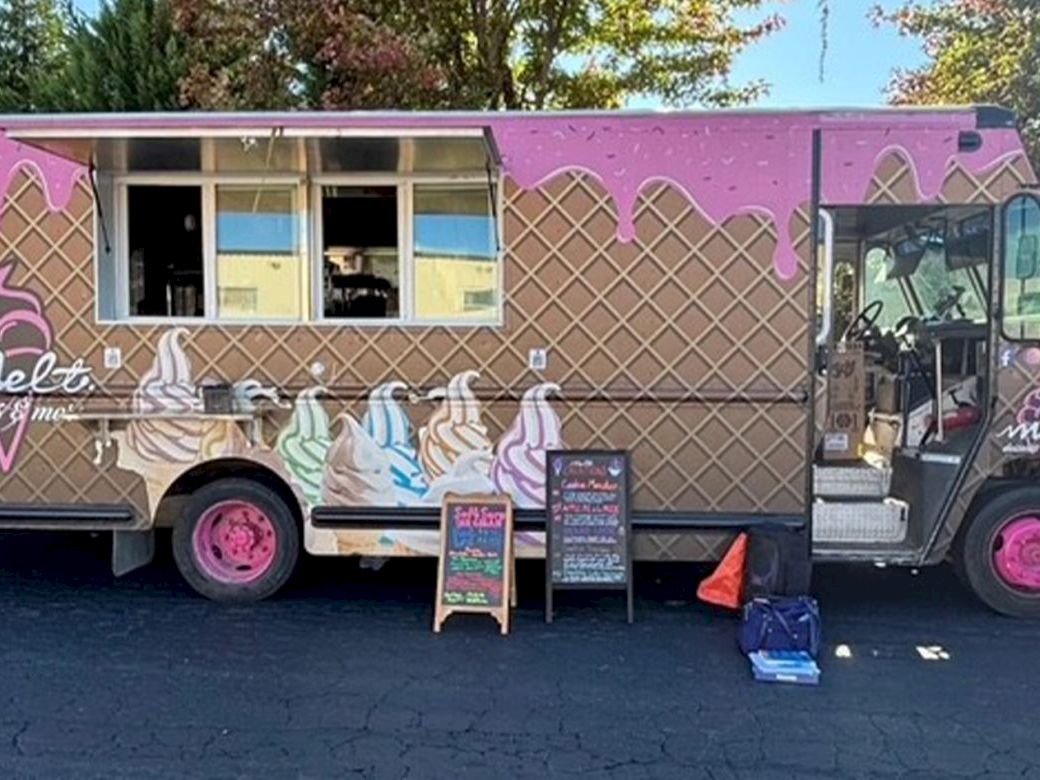 A pink-and-brown ice cream truck with a waffle cone pattern; pink wheels, ice cream art on the side, and a small chalkboard menu outside.